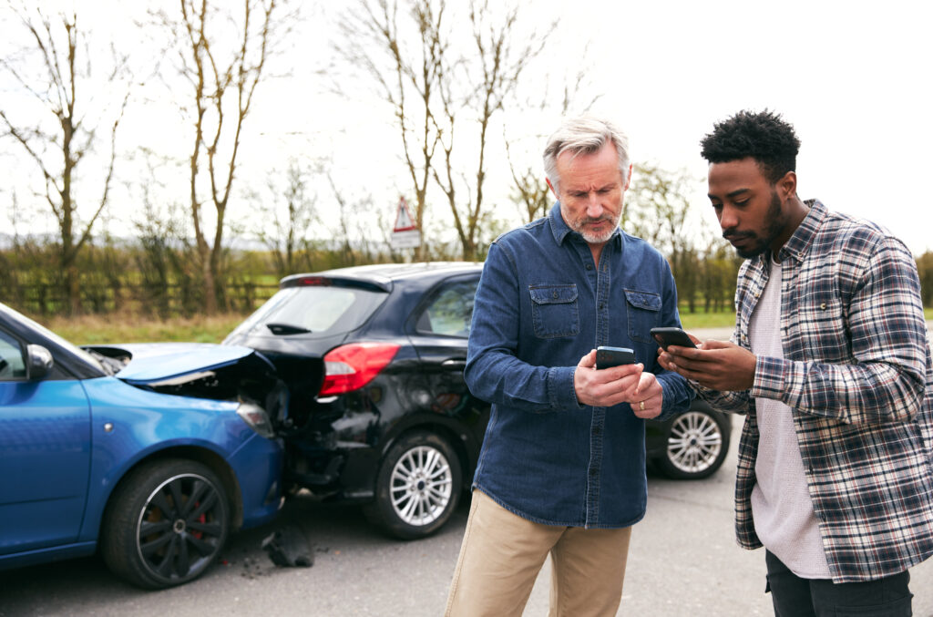 Younger and older drivers at side of the road exchanging car insurance details after traffic accident using mobile phones