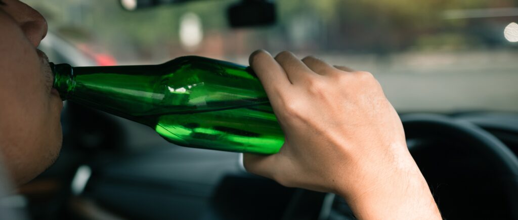 Asian men are breaking the traffic rules by holding a bottle of beer and drinking while driving.