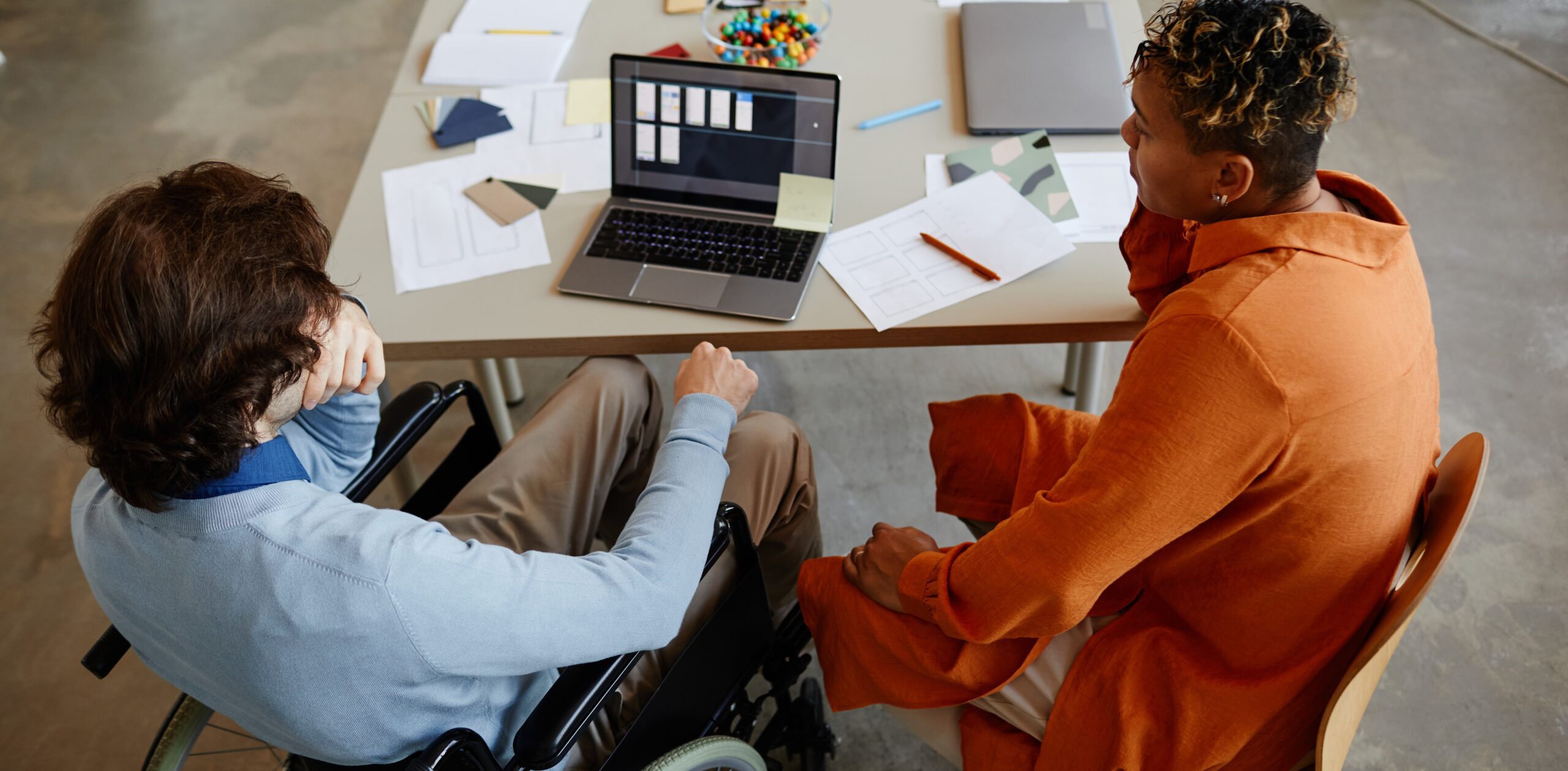 Top view of young man with disability talking to colleague or manager while working in IT development company, accessible jobs concept